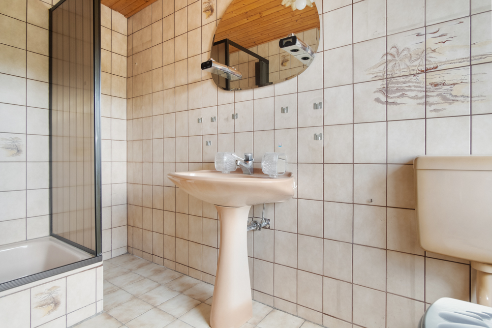 Badezimmer mit beiger Keramik, Waschbecken, Spiegel, Dusche und gemusterten Fliesen.