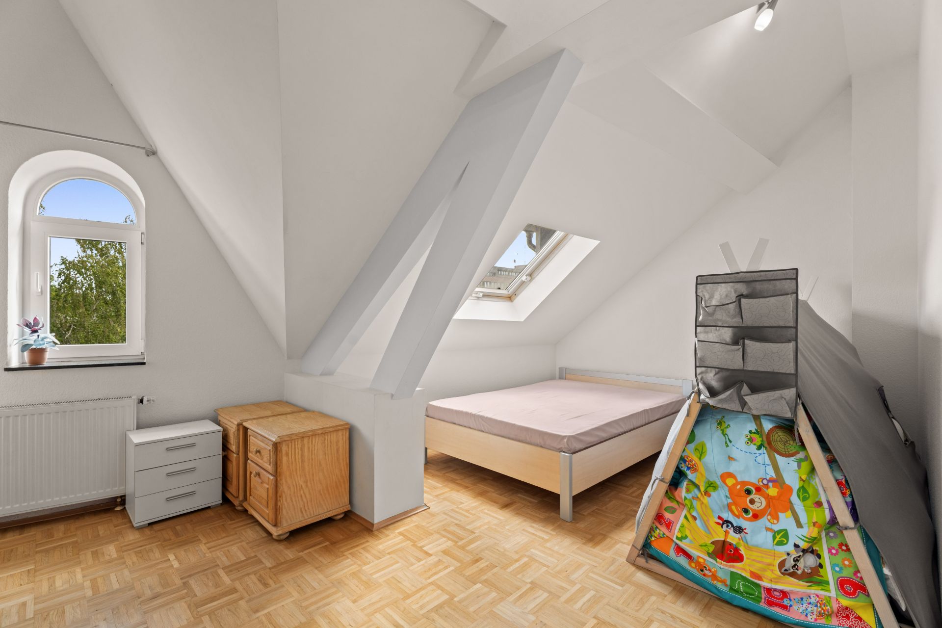 Helles Schlafzimmer mit Bett, Schränken, Dachfenster und Spielzelt im Dachgeschoss.