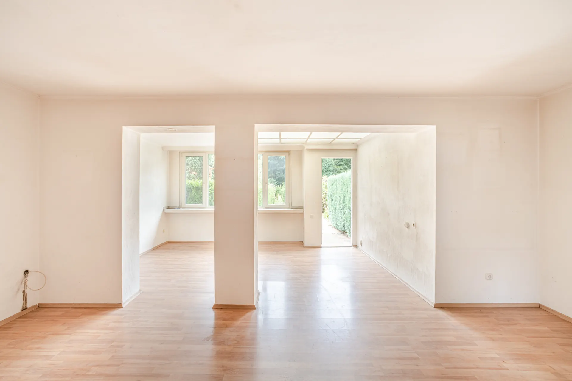 Helles, leeres Zimmer mit Holzboden, großen Fenstern und einer Tür zum Garten.