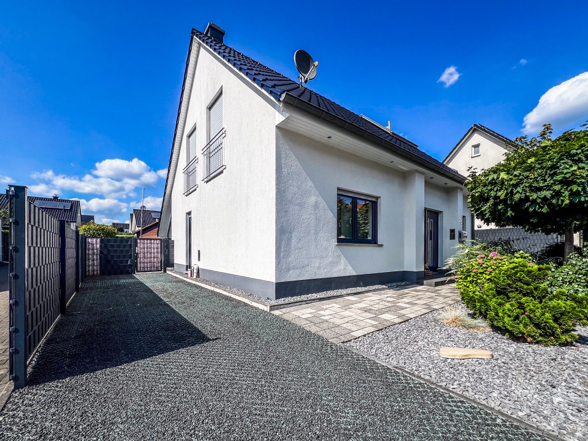 Modernes Einfamilienhaus mit hellem Putz und Vorgarten bei blauem Himmel.