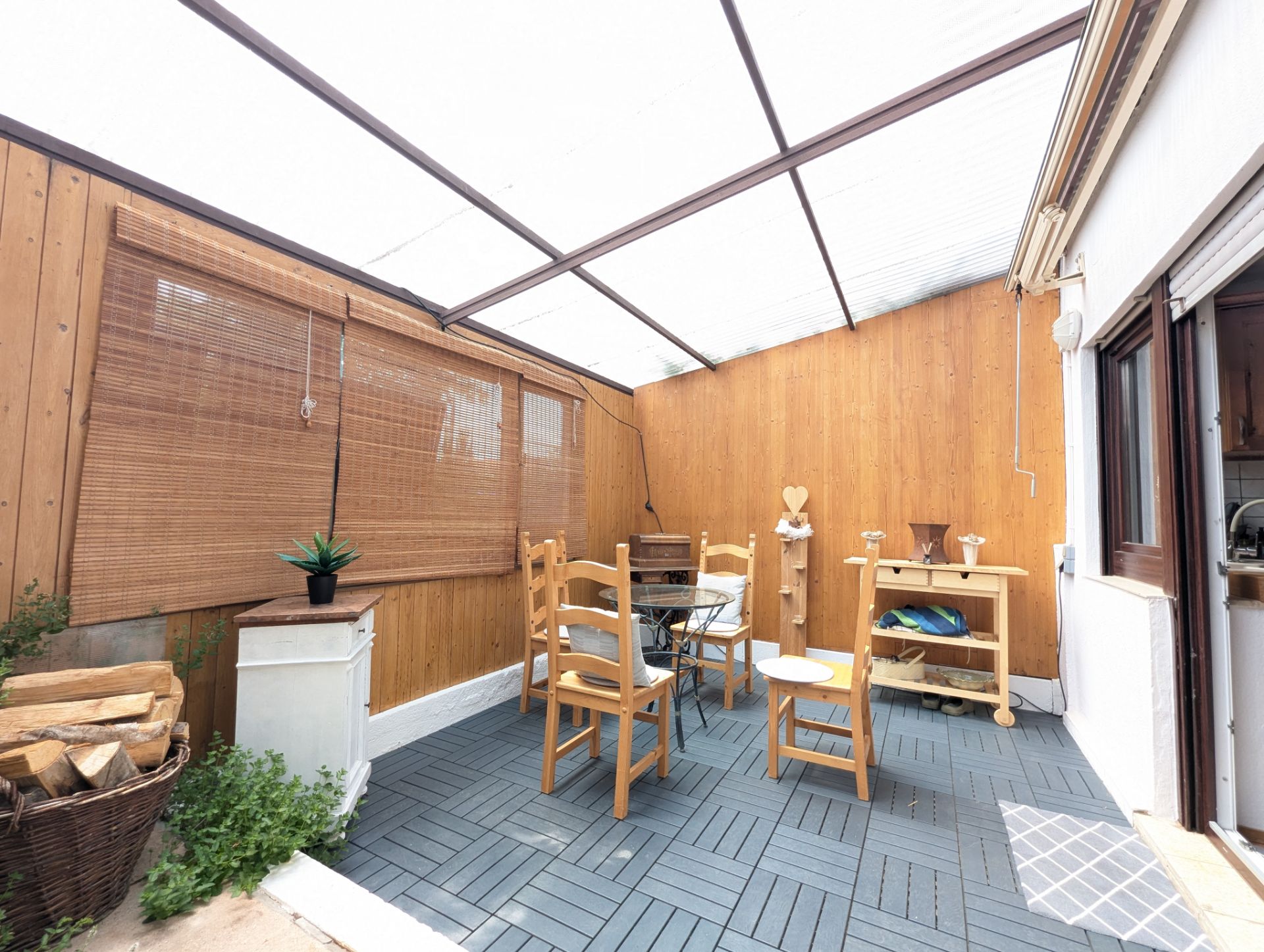 Überdachte Terrasse mit Holzwänden, Holzmöbeln und einem kleinen Tisch mit Stühlen.