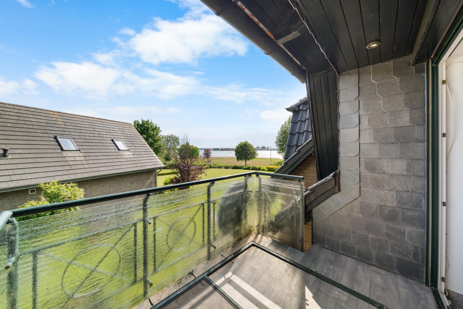 Kleiner Balkon mit Glasgeländer und Blick auf Garten und Felder.