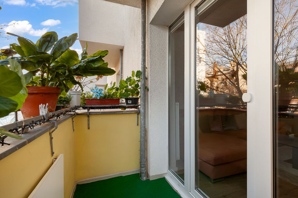 Kleiner Balkon mit Topfpflanzen, gelbem Geländer und Zugang durch eine Glastür.