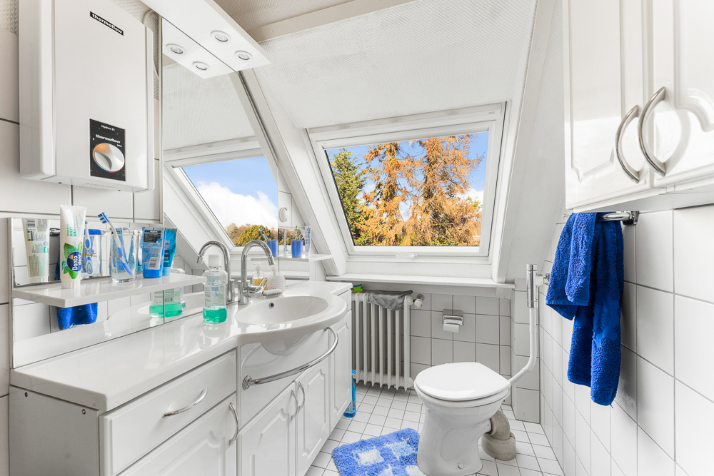 Helles Badezimmer mit Dachfenster, weißem Waschbecken, Toilette und blauen Handtüchern.