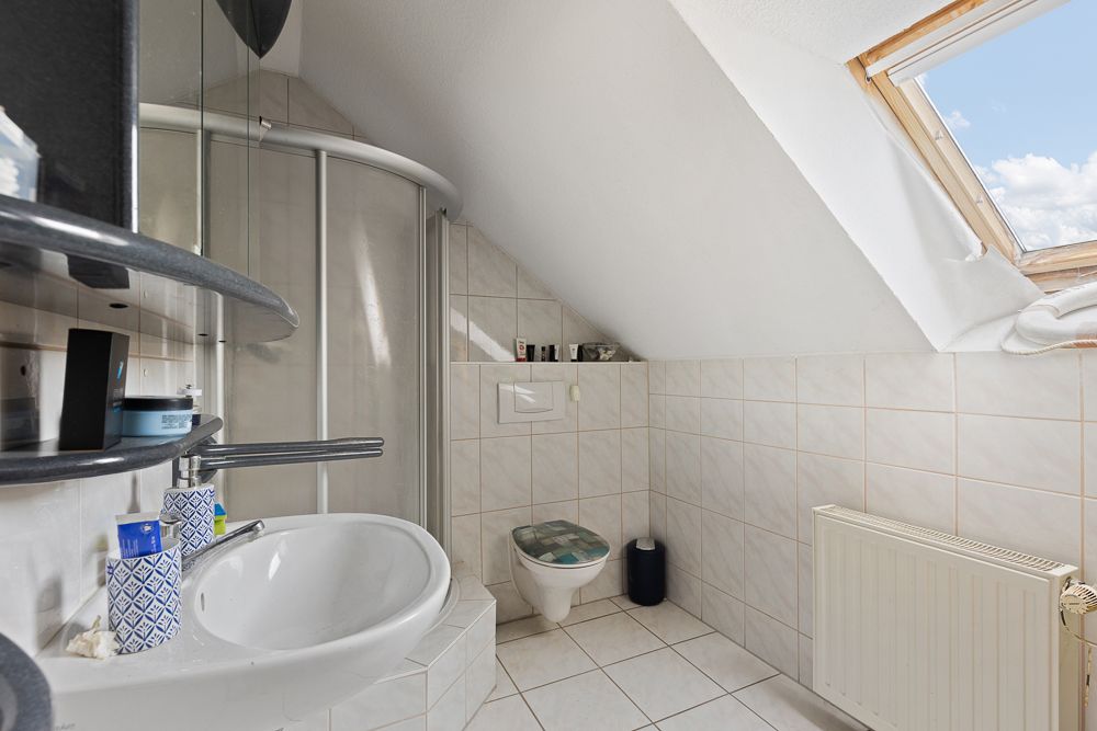 Helles Badezimmer mit Dusche, Waschbecken, Toilette und Dachfenster unter einer Schräge.