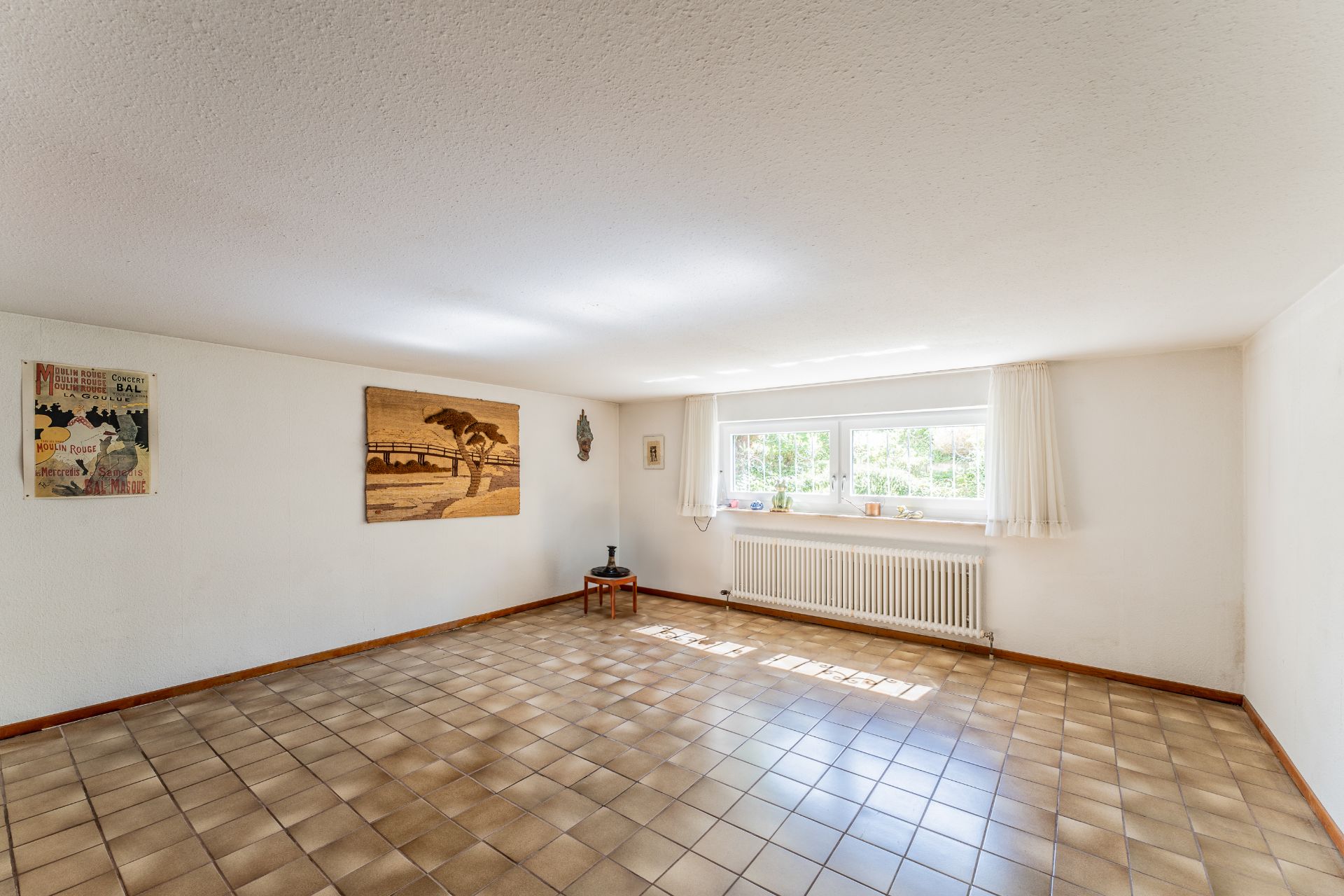 Heller Raum mit Fliesenboden, Wanddekorationen und einem Fenster mit weißem Vorhang.