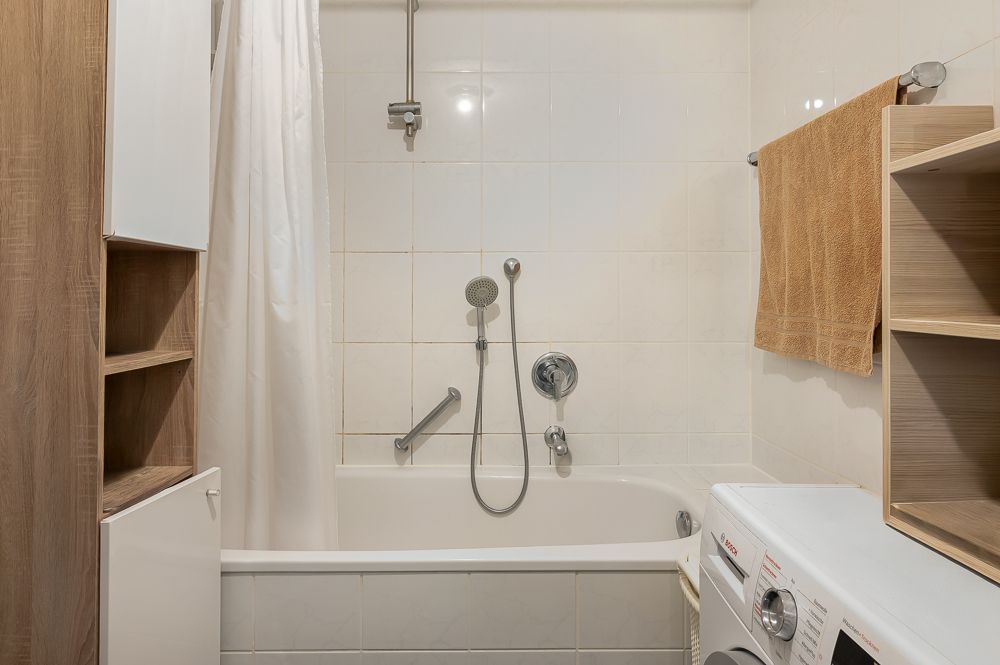 Badezimmer mit Badewanne, Duschvorhang, Waschmaschine und Regalen.
