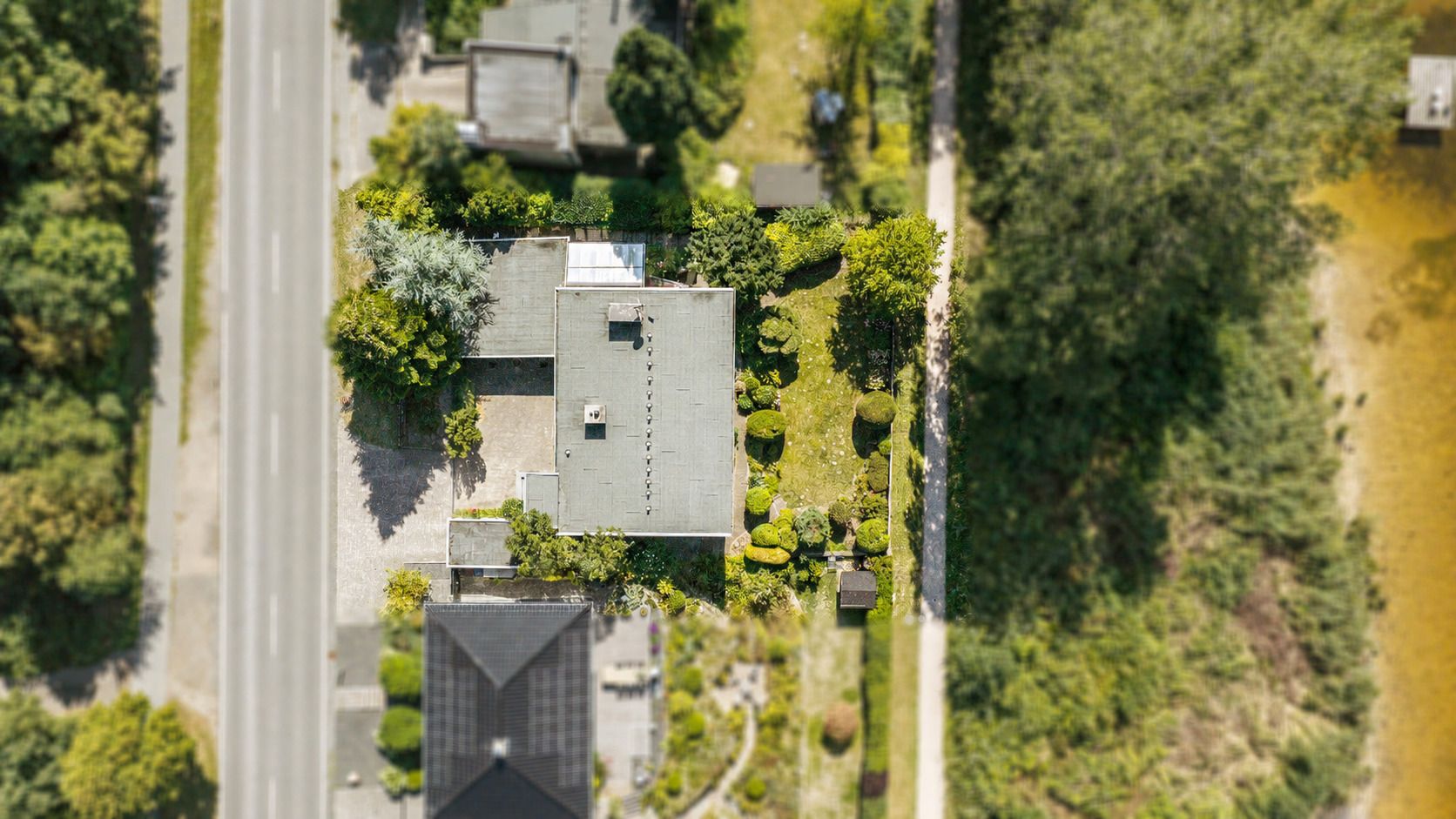 Luftaufnahme eines Wohnhauses mit Garten, angrenzend an eine Straße und viel Grün.