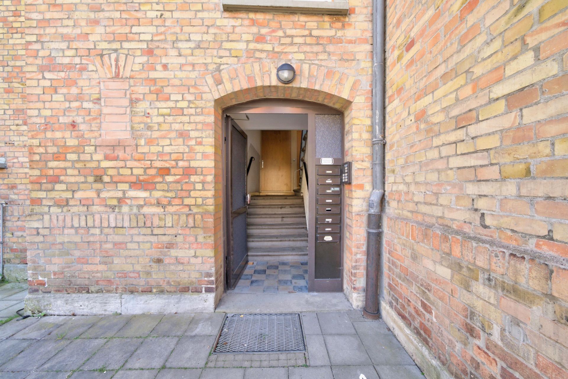 Eingang eines Wohnhauses aus Backstein mit offenen Türen, Briefkästen und Treppenhaus.