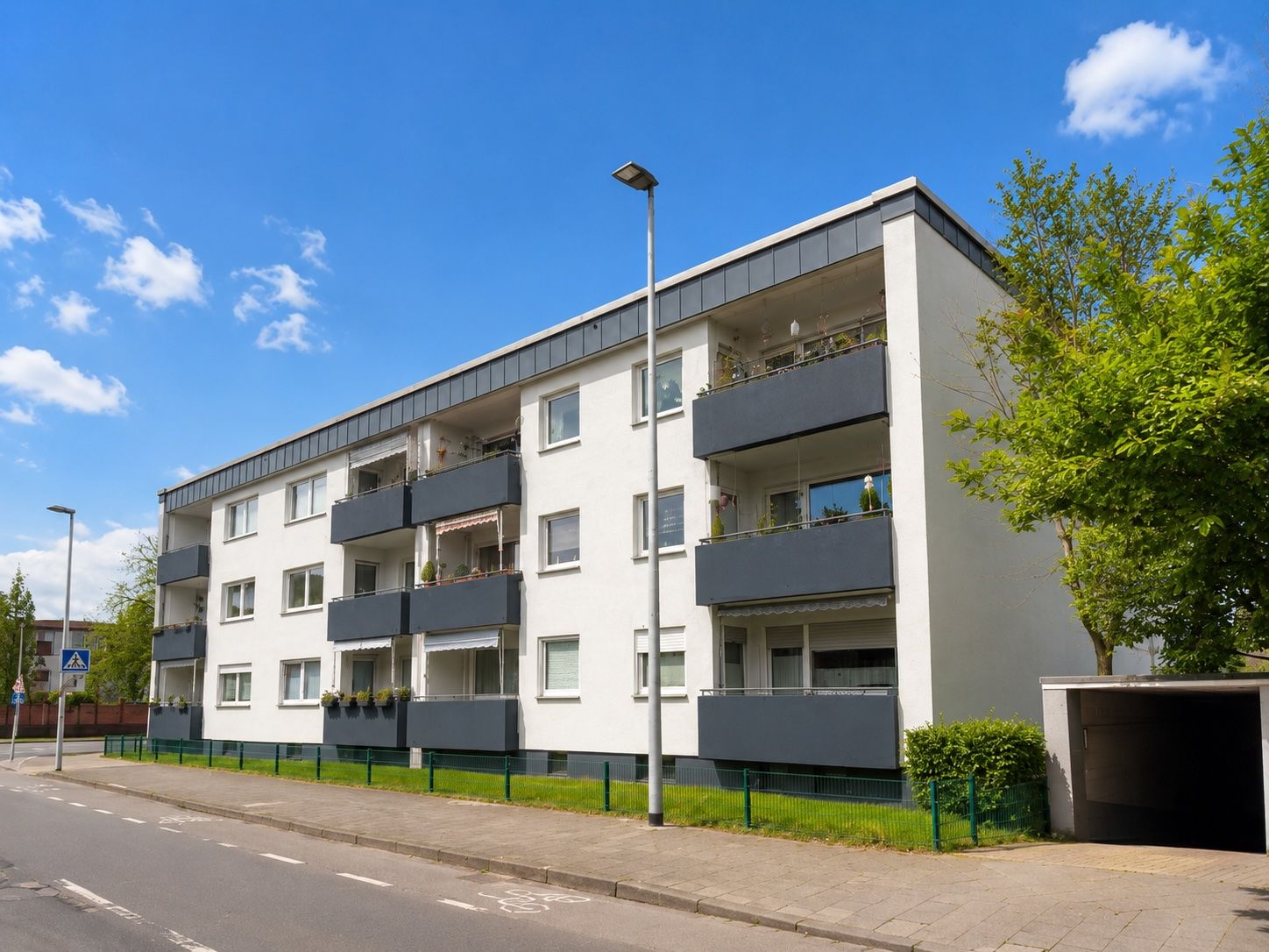 Modernes, dreistöckiges Wohnhaus mit Balkonen an einer ruhigen Straße.