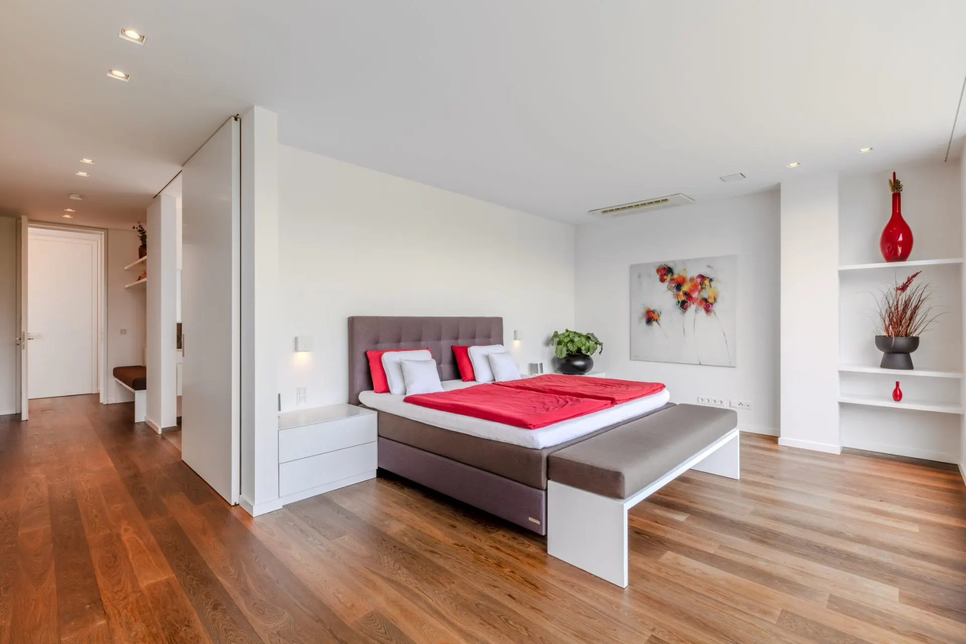 Modernes Schlafzimmer mit Doppelbett, Holzboden und dekorativen Regalen an der Wand.