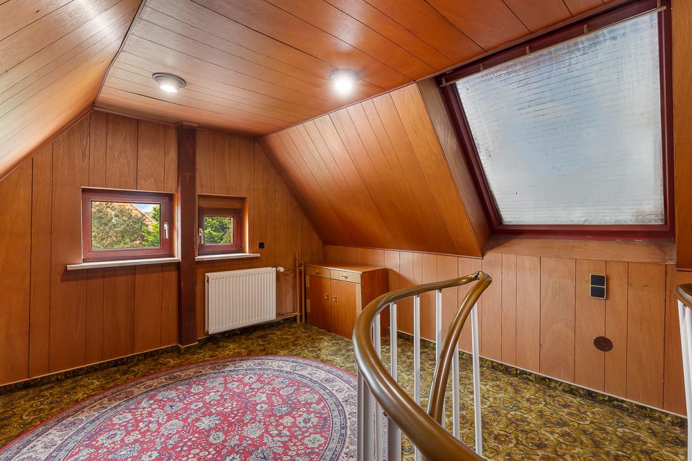 Dachgeschosszimmer mit Holzverkleidung, großem Fenster, rundem Teppich und Wendeltreppe.