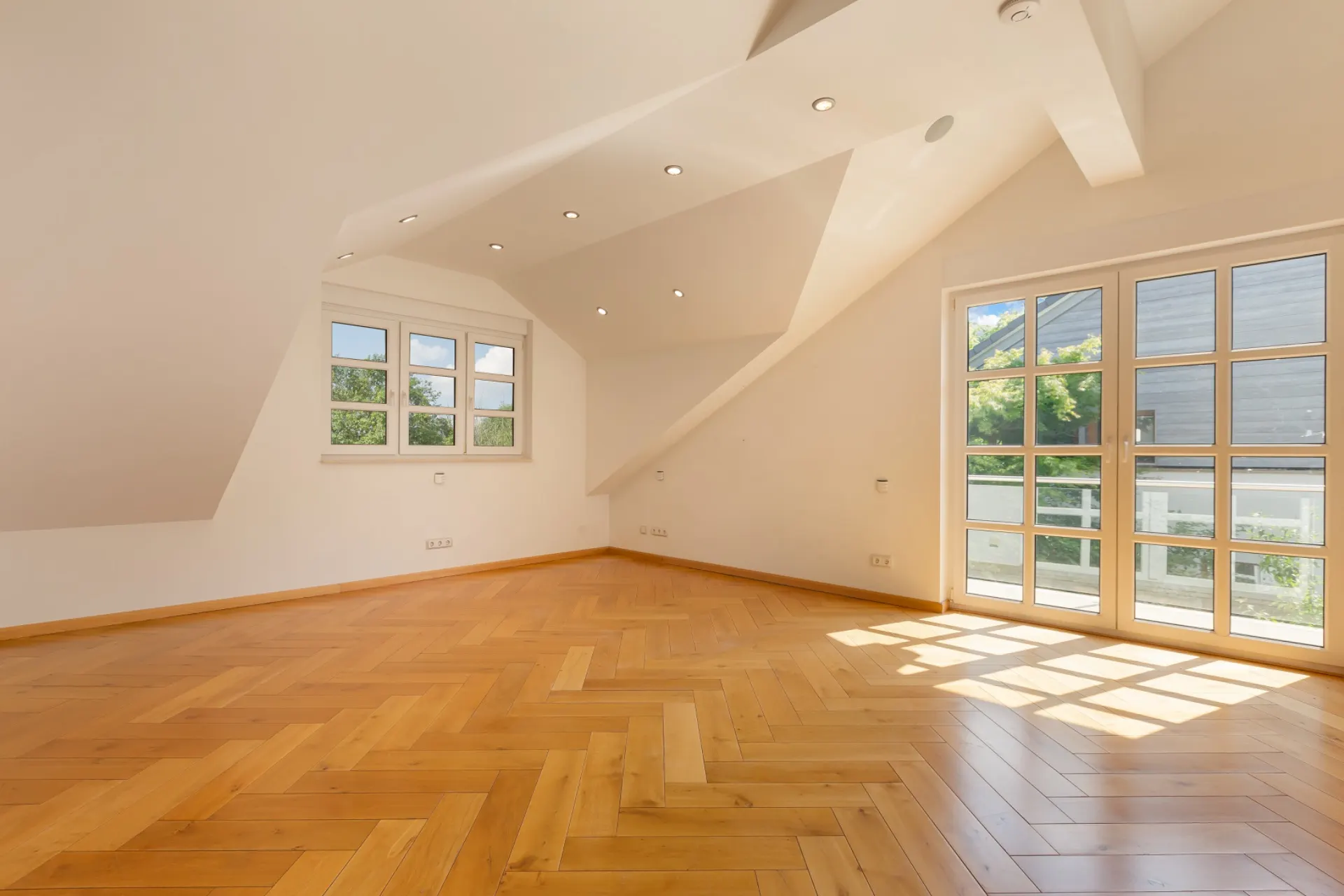 Helles Zimmer mit Holzparkett, Dachschräge, Fenstern und Glastür zur Terrasse.