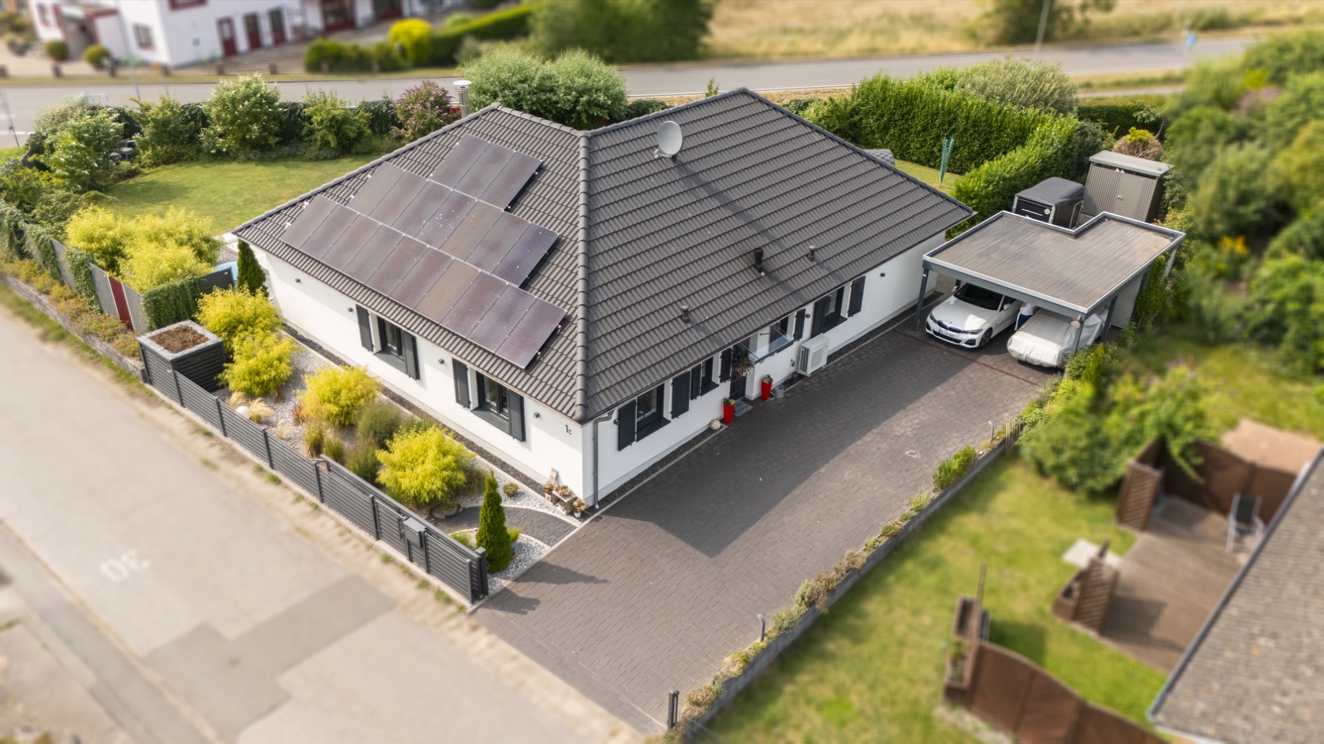 Modernes Einfamilienhaus mit Solarpanelen und Doppelcarport, umgeben von Garten und Einfahrt.