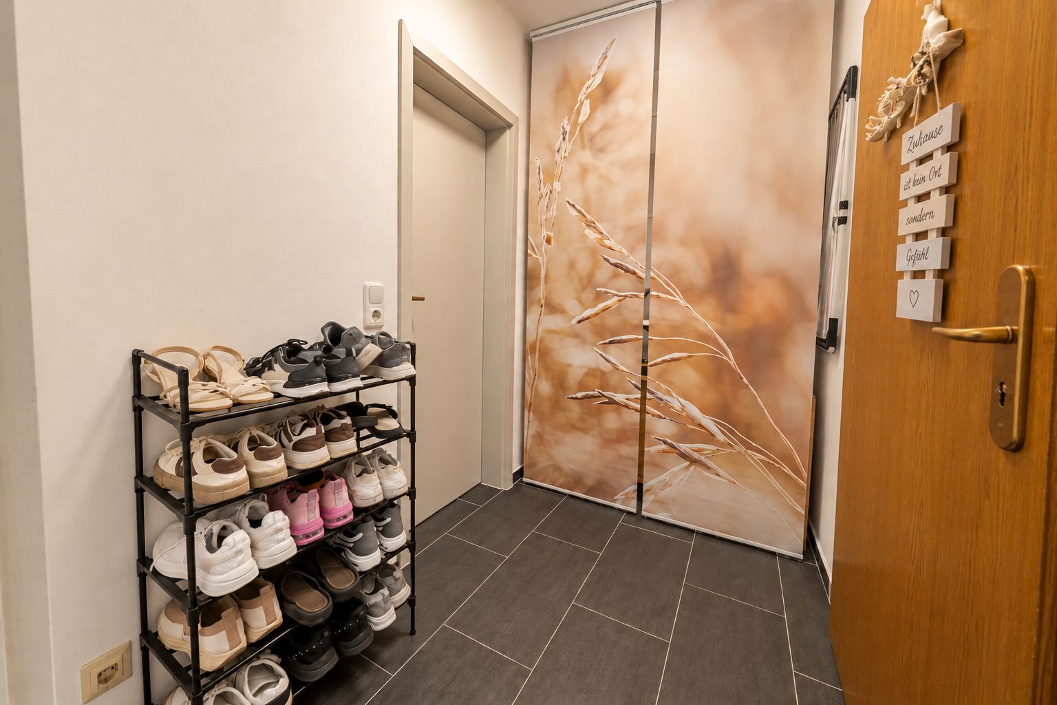 Flur mit Schuhregal, grauen Fliesen und Schiebetür mit Naturmotiv.