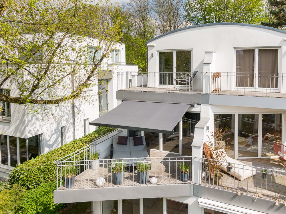 Moderne weiße Wohnhausfassade mit zwei großen Balkonen und Glasfronten im Grünen.