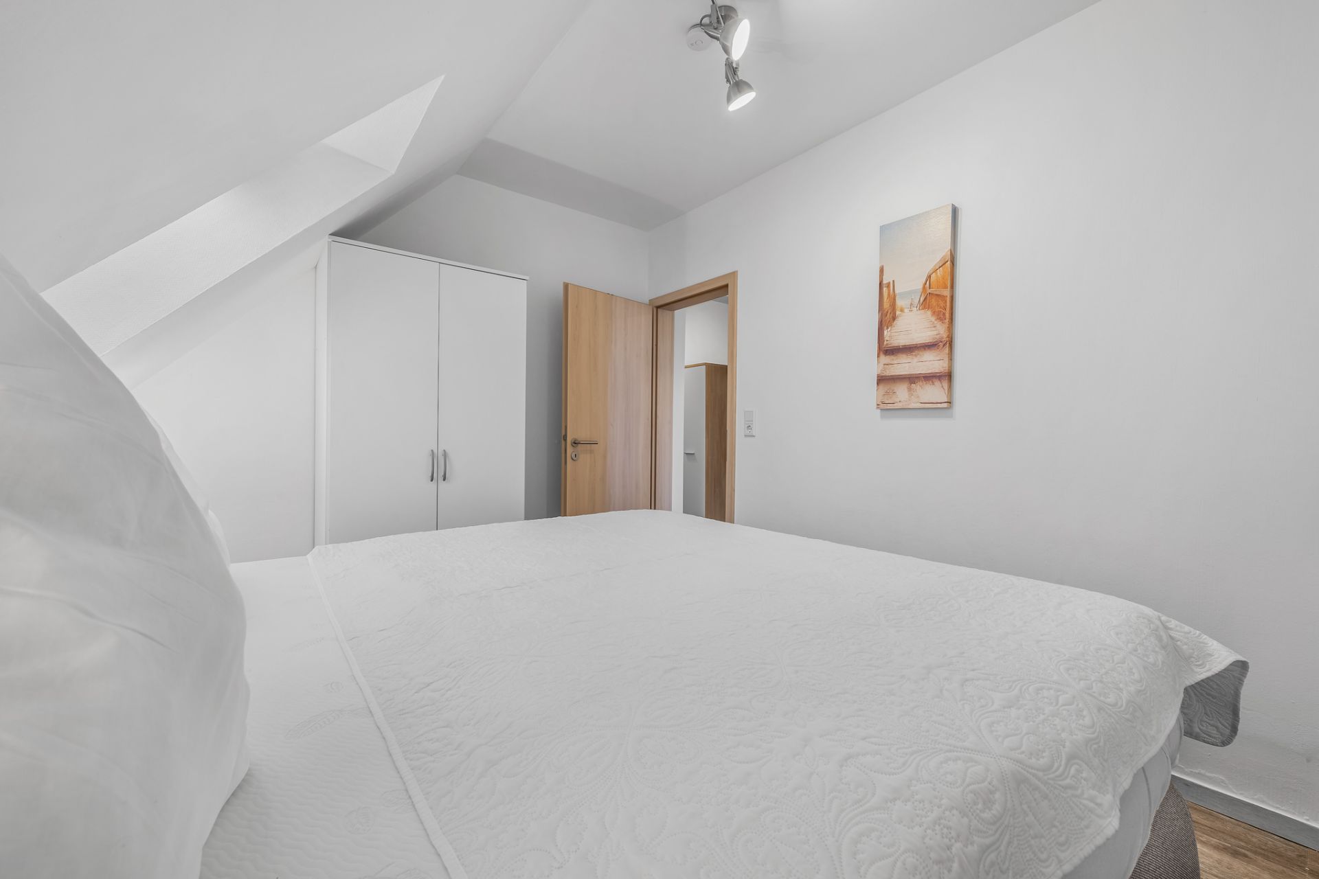 Helles Schlafzimmer mit großem Bett, weißem Schrank und Bild an der Wand.