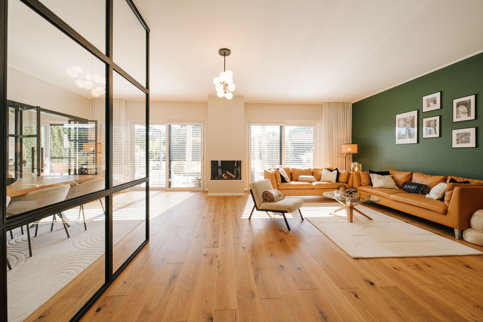 Modernes Wohnzimmer mit Holzfußboden, großer Sofaecke, Glastrennwand und viel Tageslicht.