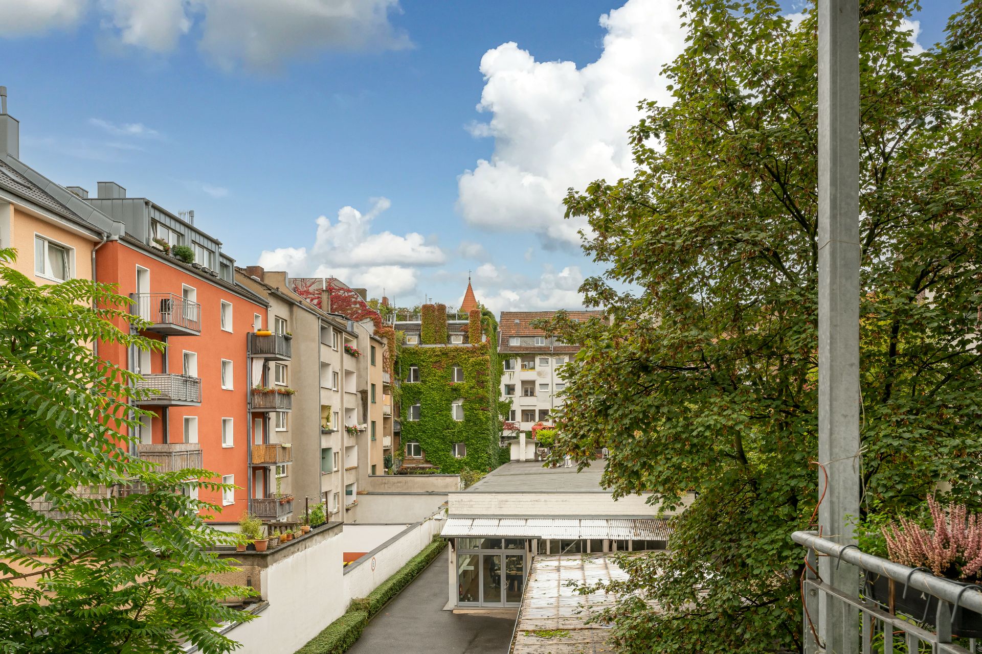 Blick auf bunte Wohngebäude mit Balkonen und Bäumen, unter blauem Himmel mit Wolken.
