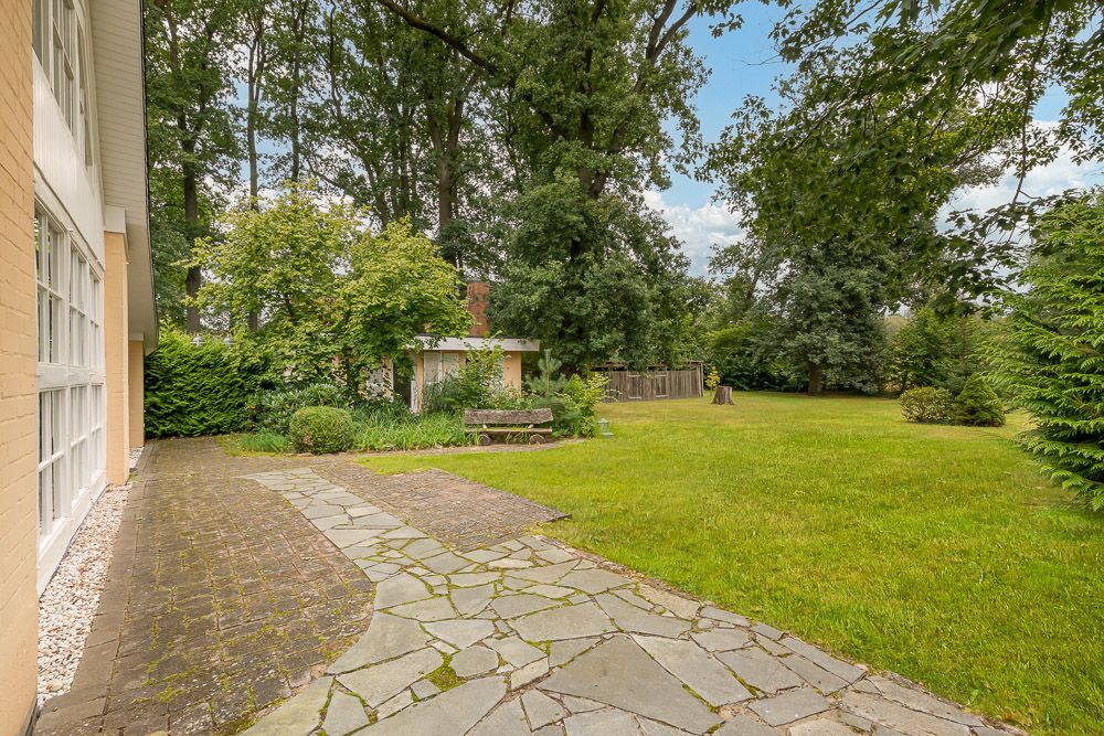 Garten mit Rasen, Steinweg, Bäumen und einem Holztisch mit Bänken neben dem Haus.