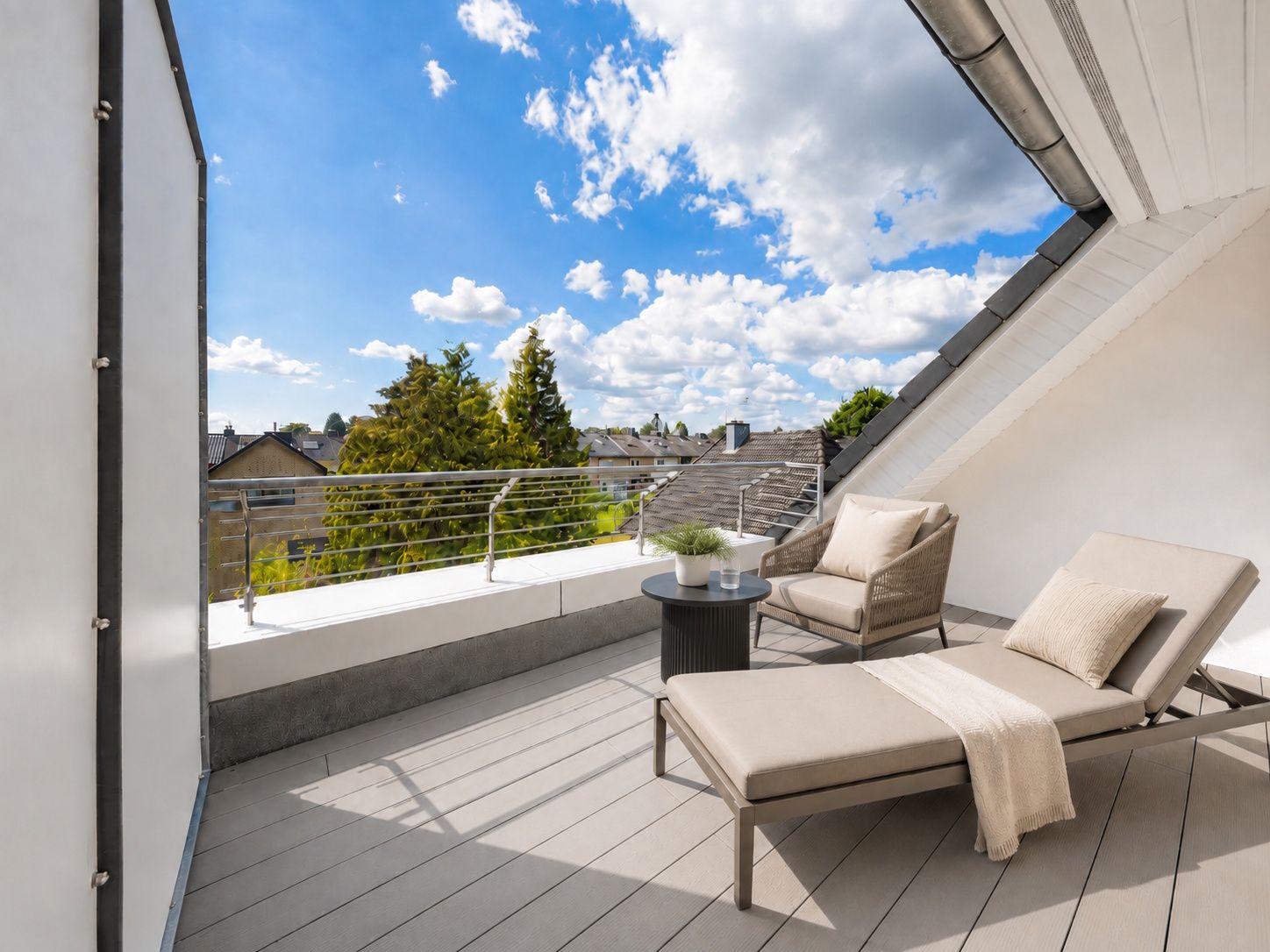 Helle Terrasse mit zwei Liegen, einem Sessel und einem kleinen Tisch mit Pflanzen unter blauem Himmel.