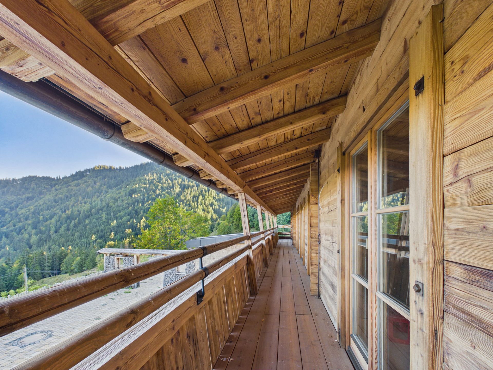Überdachter Holzbalkon mit Blick auf bewaldete Berge und große Fenster.