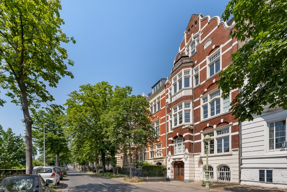 Rote Backsteinwohngebäude mit weißen Fenstern an einer von Bäumen gesäumten Straße.