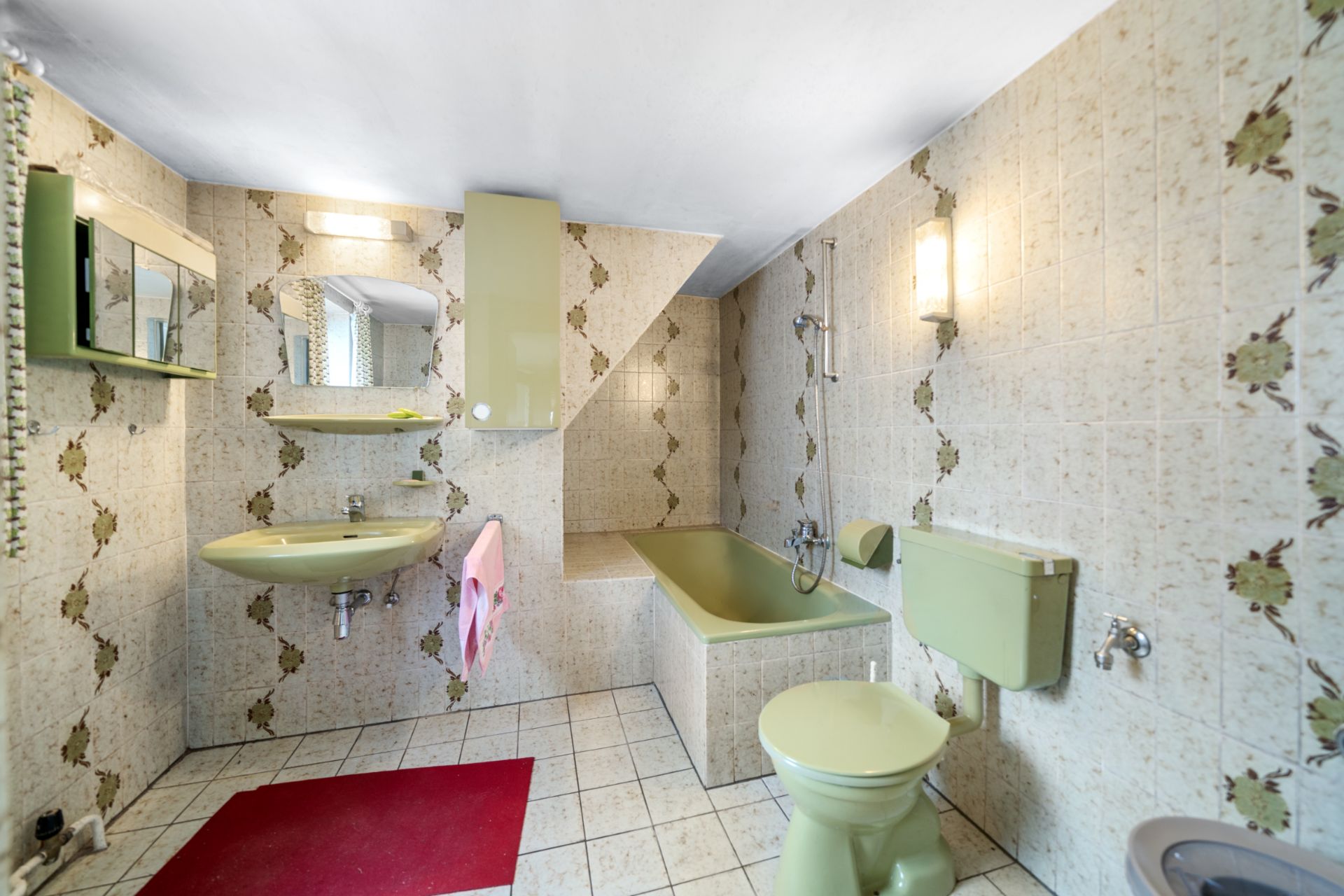 Badezimmer mit grüner Badewanne, WC, Waschbecken und gemusterten Fliesen.