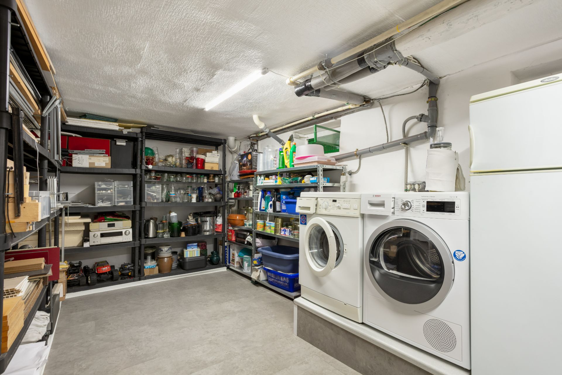 Hauswirtschaftsraum mit Waschmaschine, Trockner, Regalen und Reinigungsmitteln.