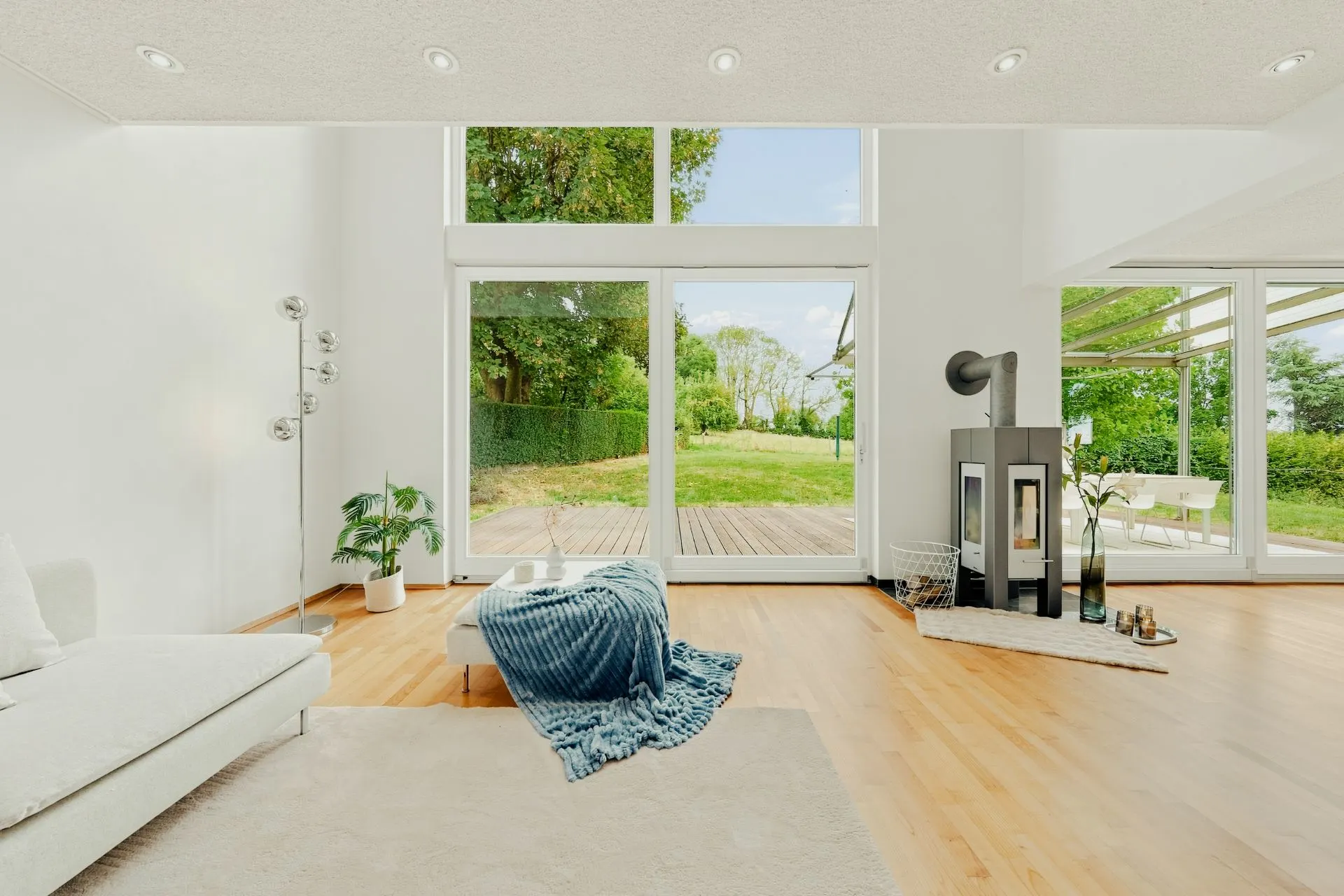 Helles Wohnzimmer mit großer Glasfront, Sofa, Ofen und Blick auf Terrasse und Garten.