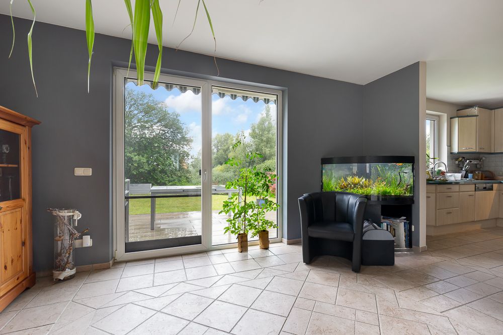 Helles Wohnzimmer mit großen Fenstern, Pflanzen, Aquarium und Blick auf den Garten.