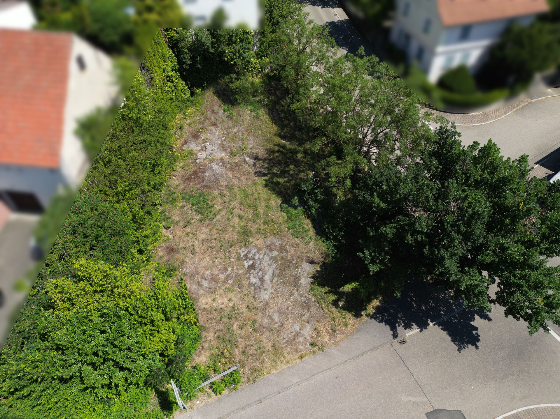 Leeres, rechteckiges Grundstück von oben, umgeben von Büschen, Bäumen und Straßen.