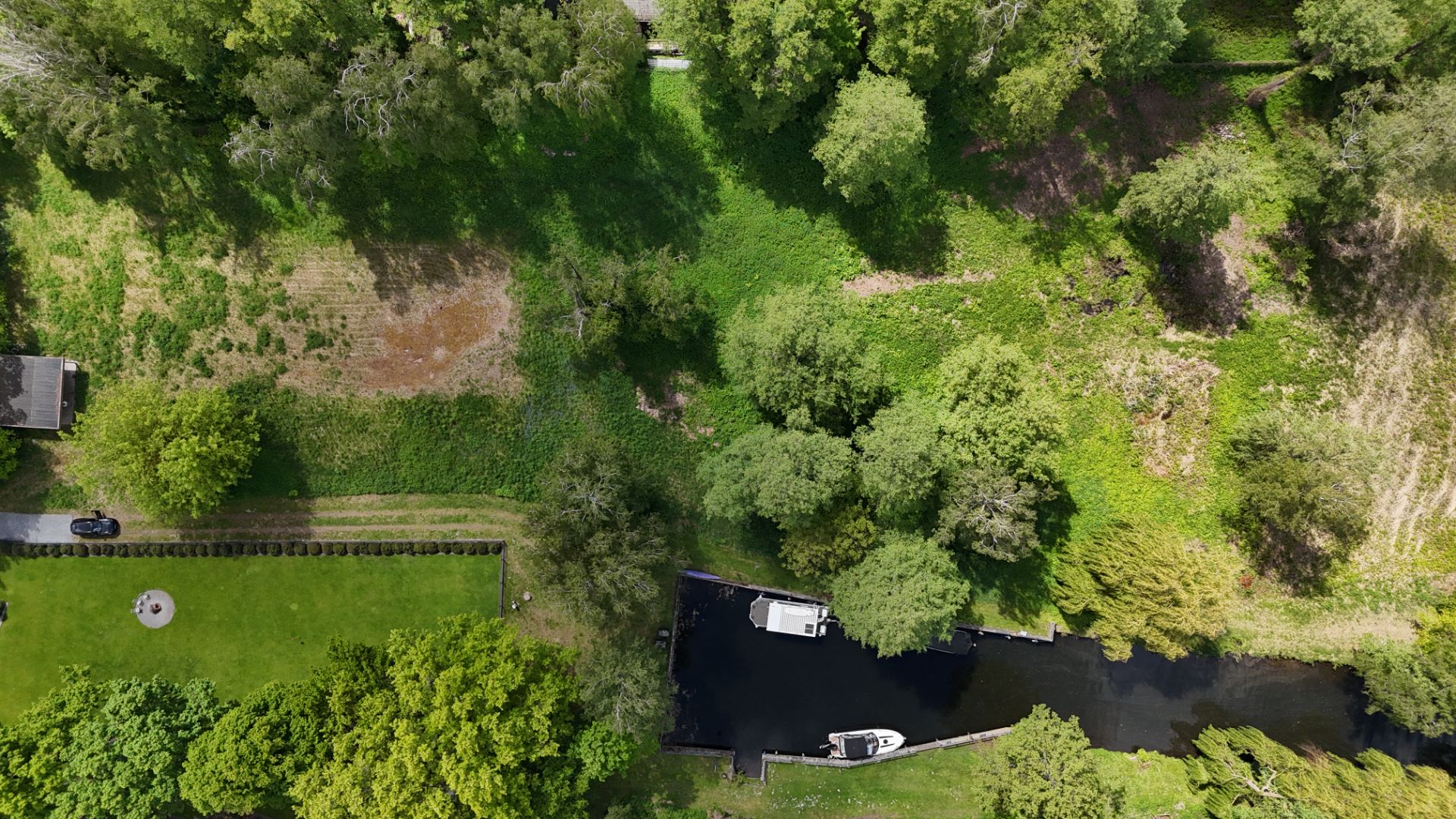 Luftbild von Grundstück mit viel Grünfläche, Bäumen, einem Kanal und zwei Booten.
