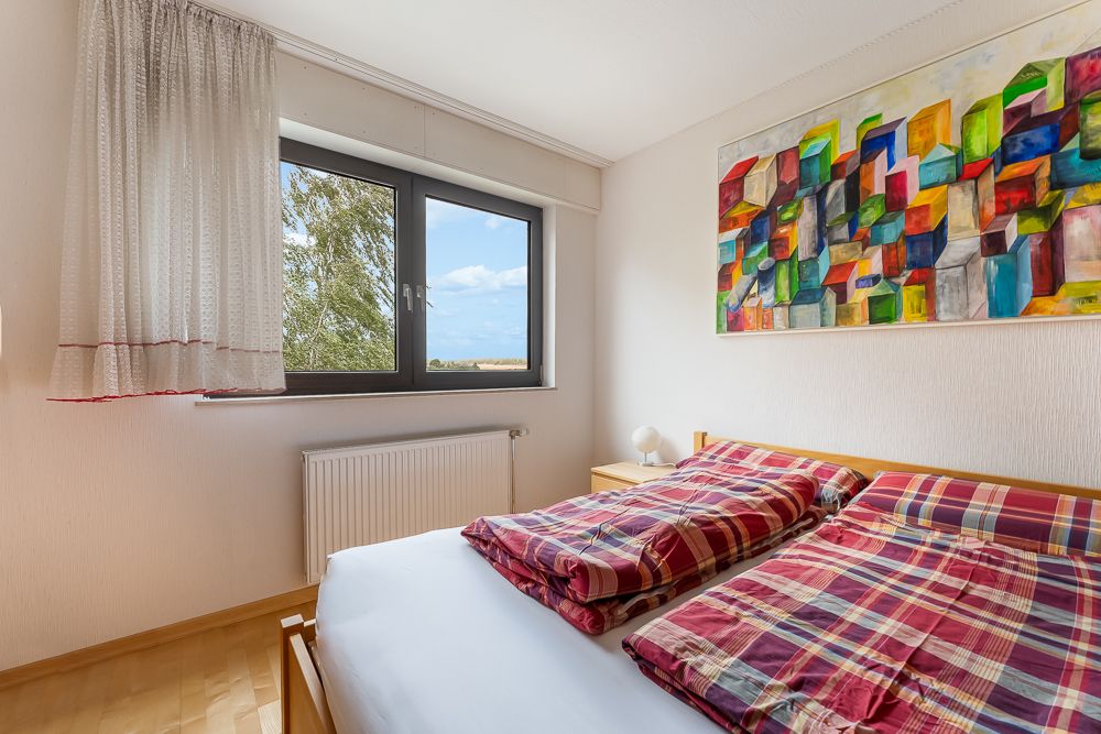 Helles Schlafzimmer mit Doppelbett, karierten Bettdecken, Fenster und buntem Wandbild.