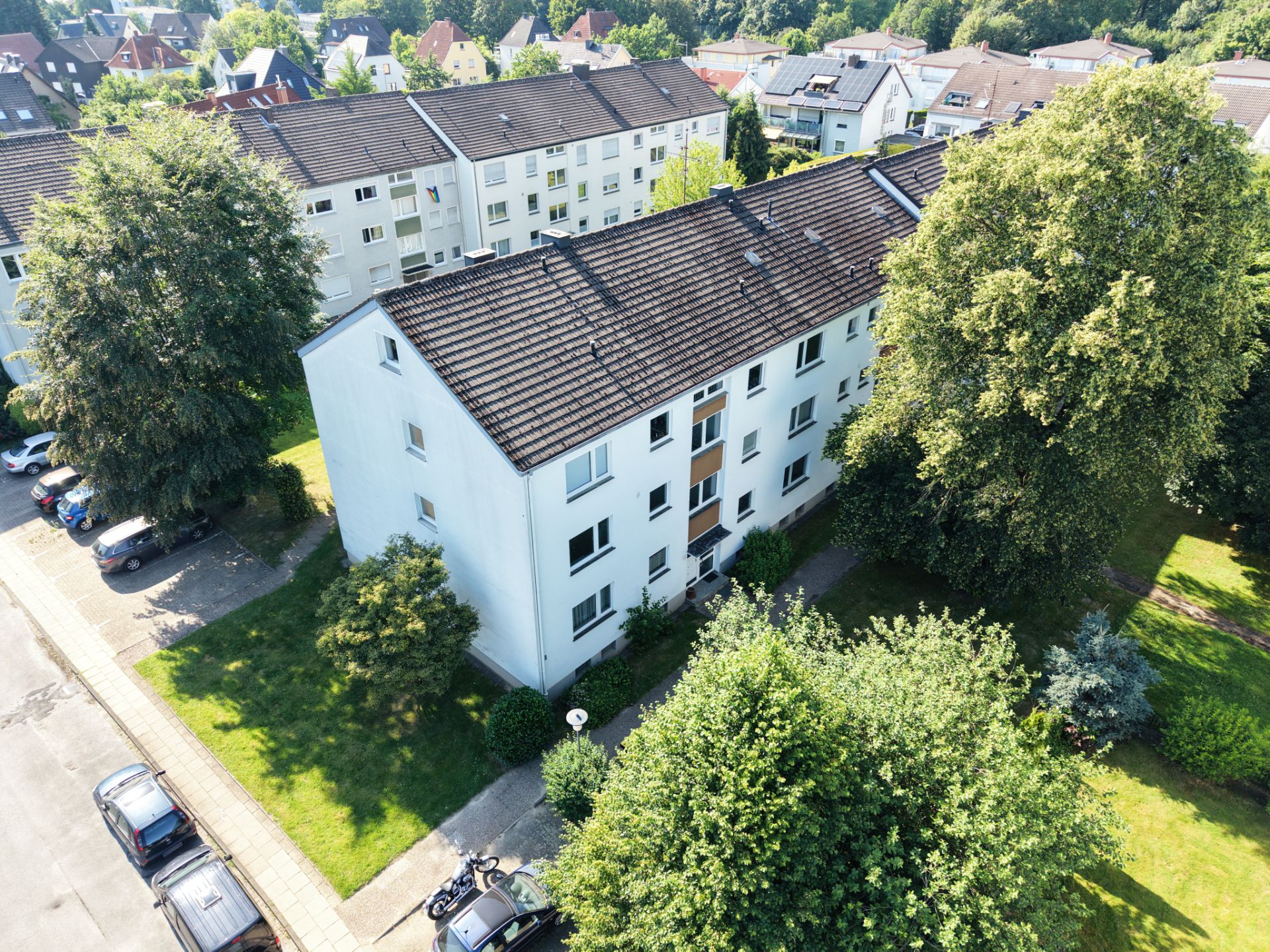 Mehrfamilienhaus mit weißer Fassade, umgeben von Bäumen und Grünflächen.
