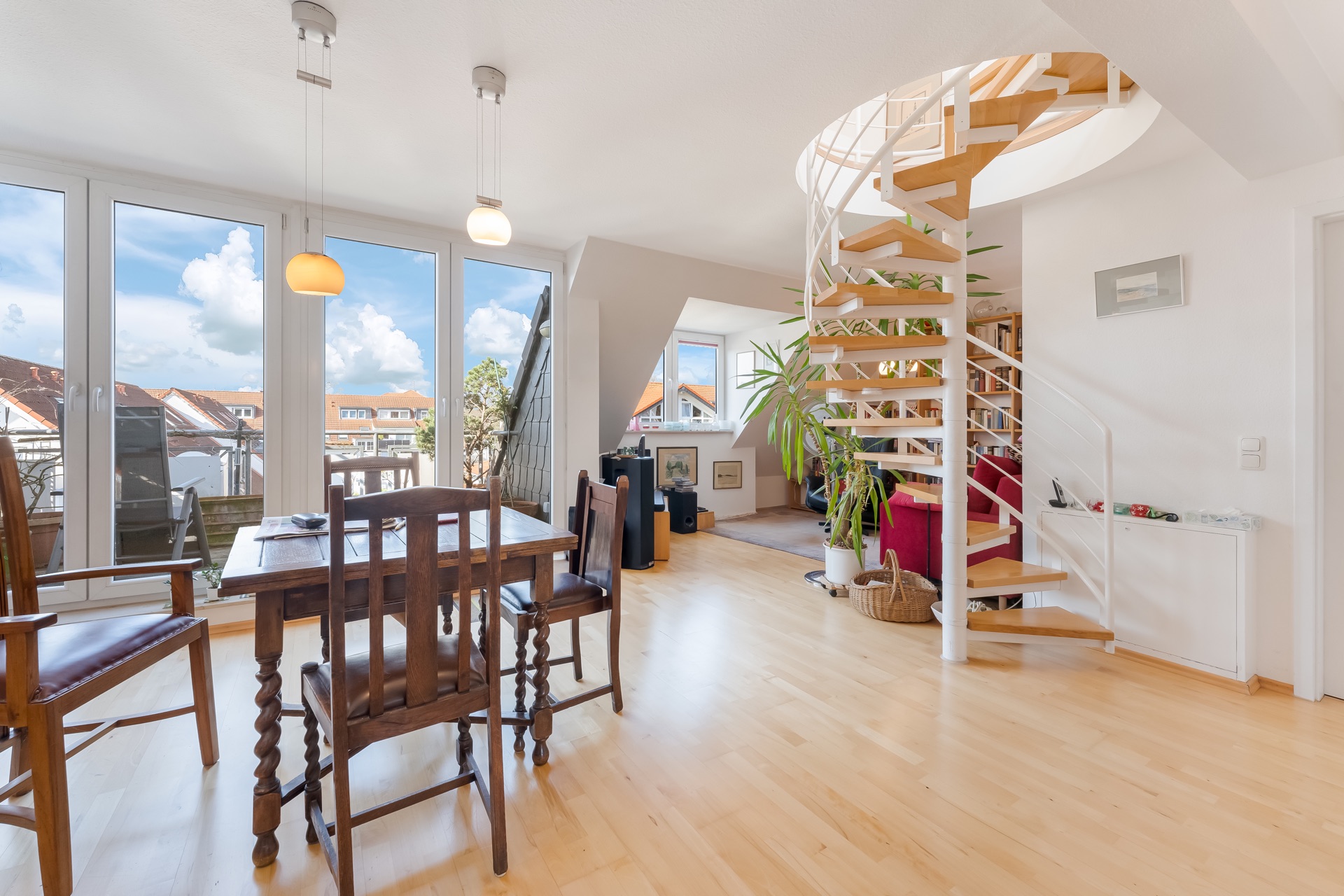 Helles Wohnzimmer mit Holztreppe, Esstisch, Stühlen und großen Fenstern zum Balkon.