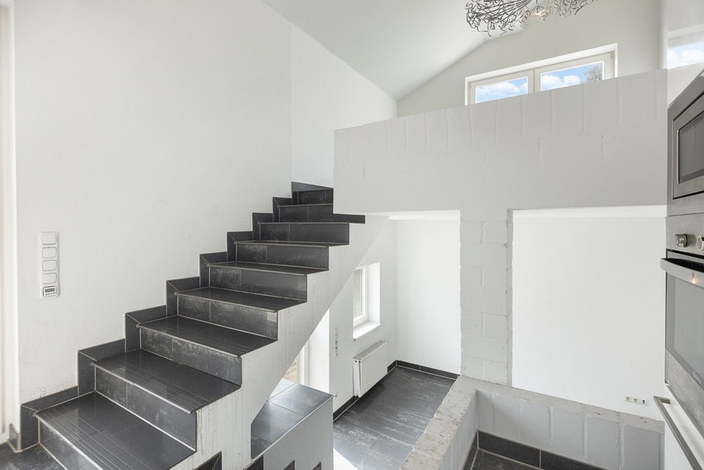 Moderne schwarze Treppe in hellen Wohnräumen mit weißen Wänden und großen Fenstern.