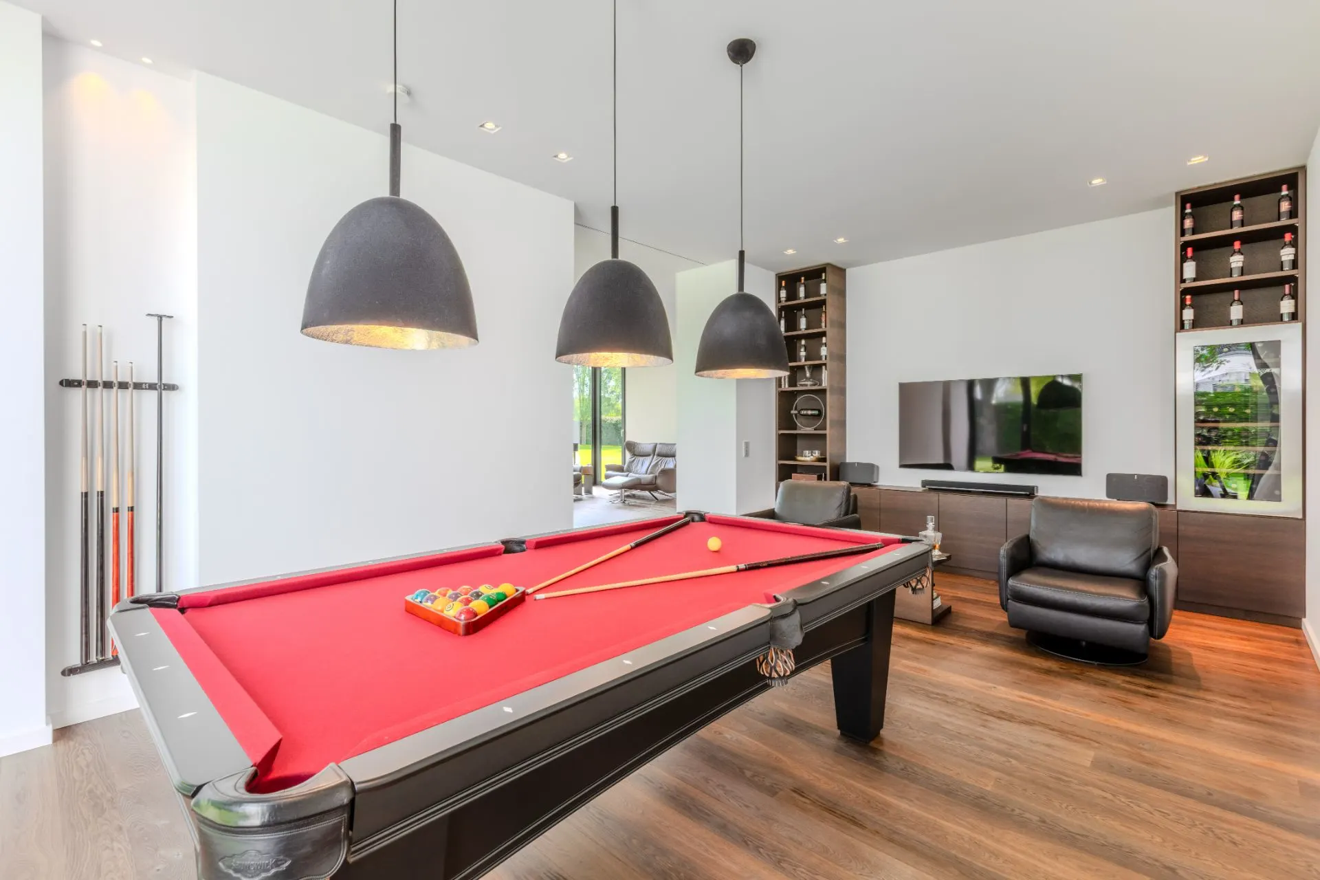 Modernes Wohnzimmer mit Billardtisch, Fernseher, Ledersesseln und Holzfußboden.