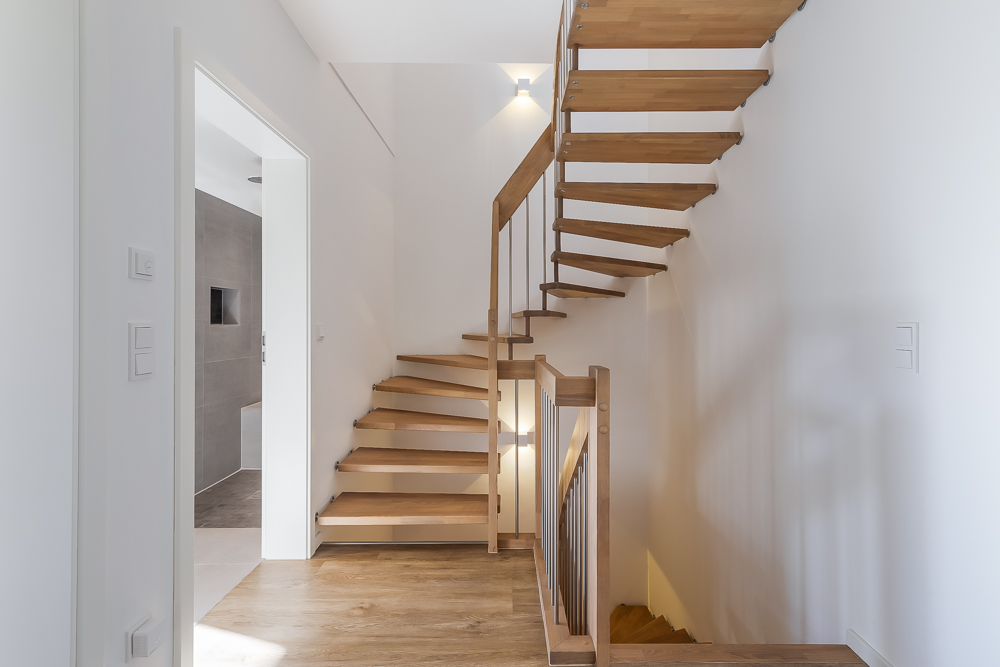 Helle Diele mit moderner Holztreppe und Blick in ein angrenzendes Badezimmer.