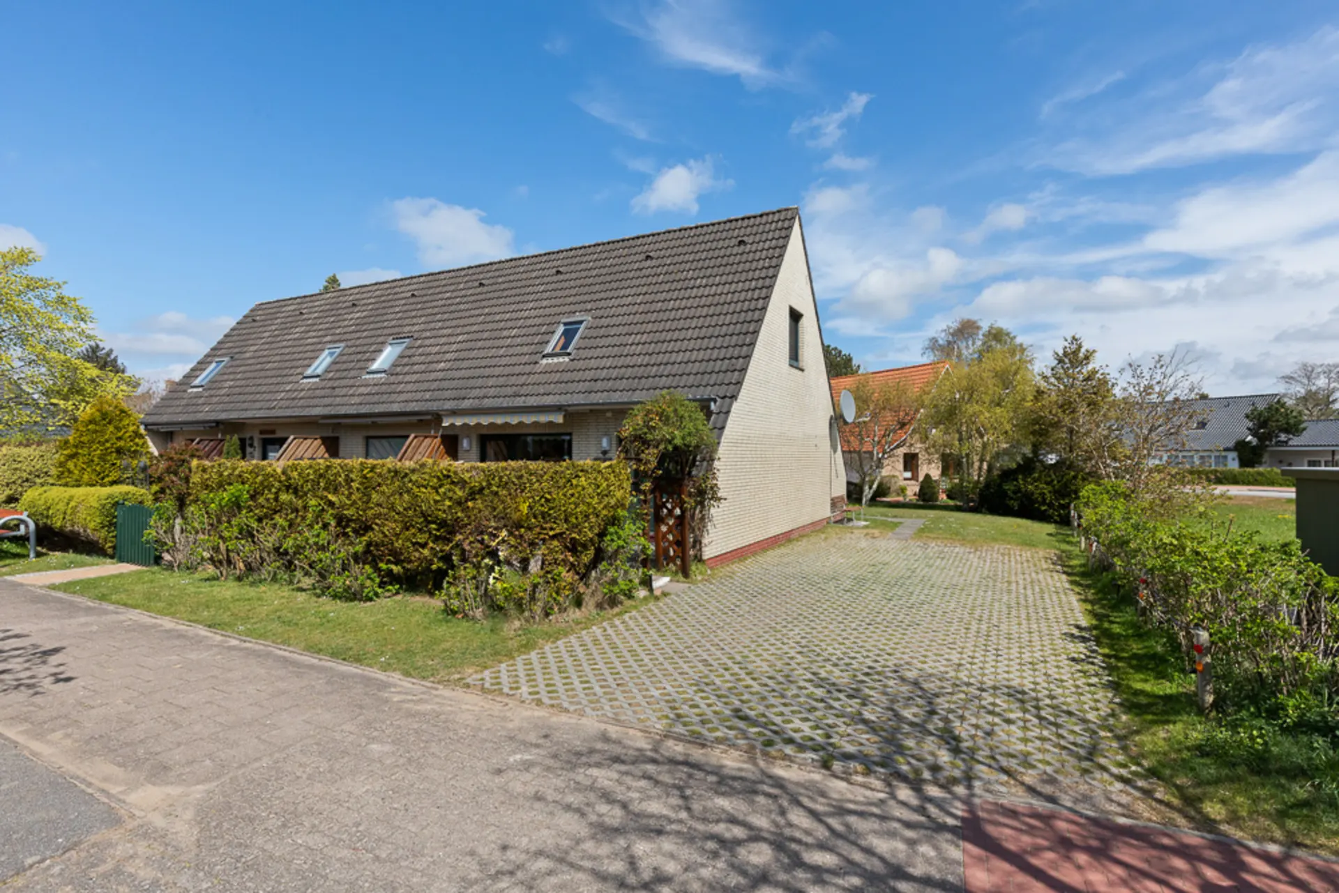 Doppelhaushälfte mit Dachfenstern, großer Einfahrt und gepflegtem Garten bei sonnigem Wetter.