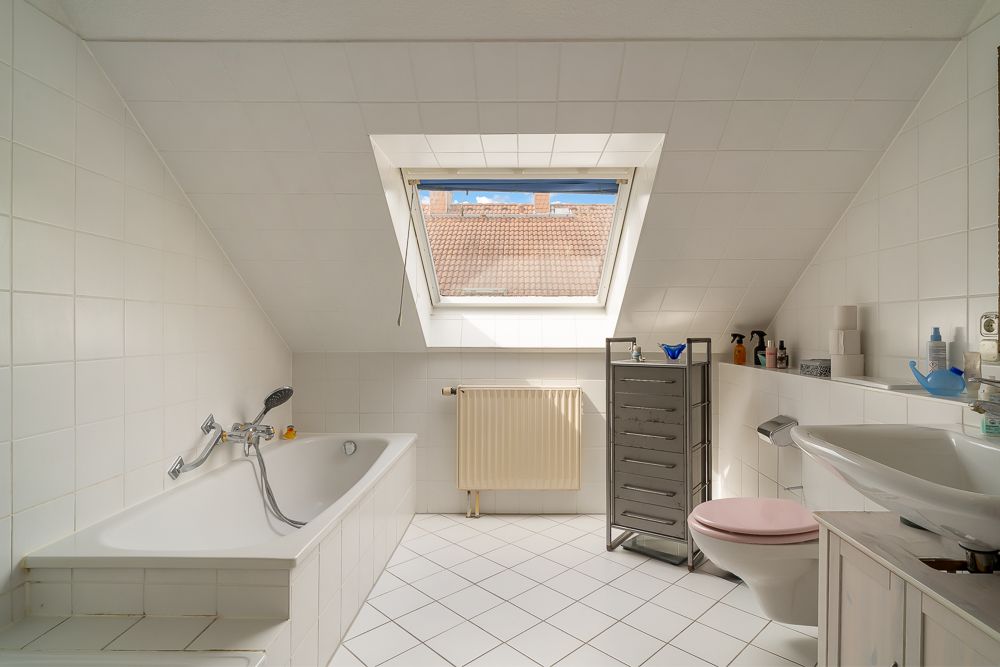 Helles Badezimmer mit Badewanne, Dachfenster, Waschbecken und WC unter einer Schräge.
