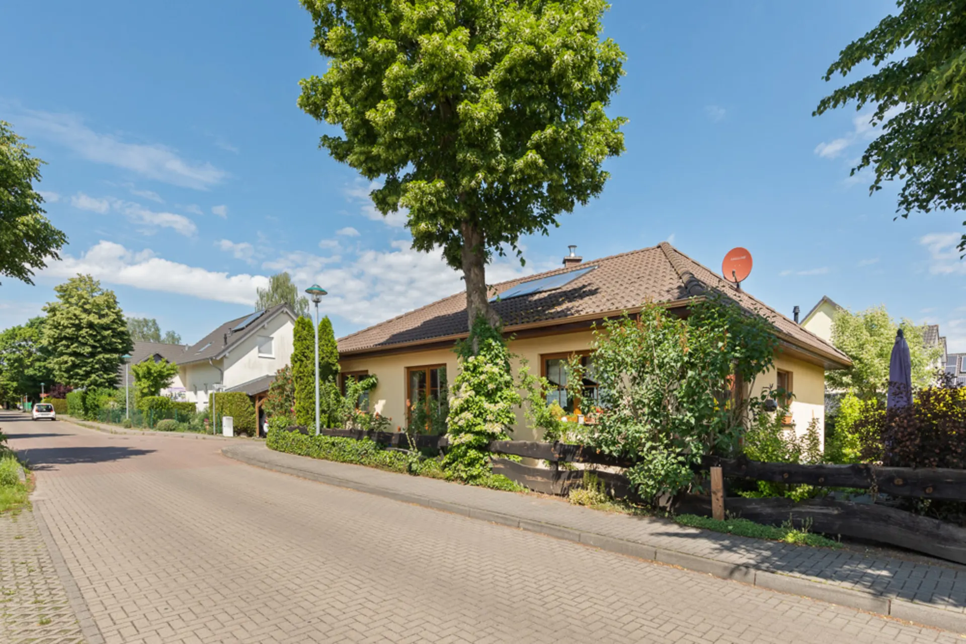 Ein Einfamilienhaus mit Garten und Bäumen an einer ruhigen Wohnstraße.