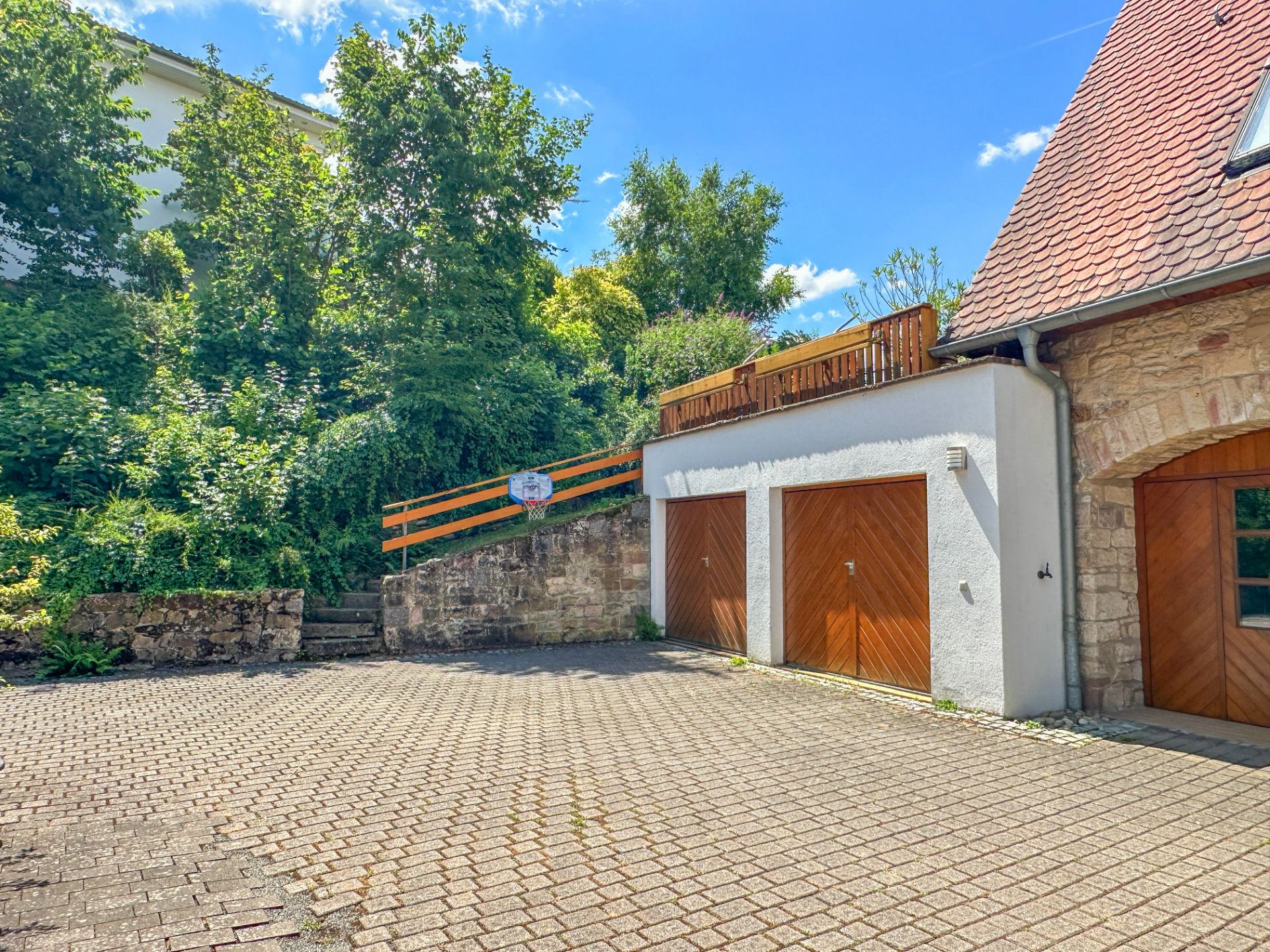 Zwei Garagentore und ein gepflasterter Hof neben einem begrünten Hang.