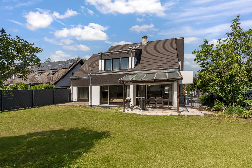 Modernes Einfamilienhaus mit Terrasse und großem Garten, umgeben von Bäumen und Nachbarhäusern.