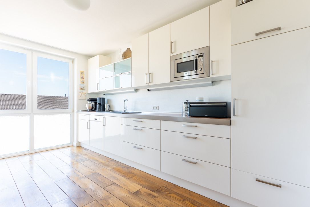Helle, moderne Küche mit weißen Schränken, Holzfußboden und großen Fenstern.