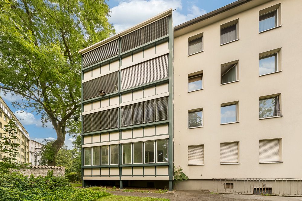 Mehrfamilienhaus mit mehreren Etagen und großen Fenstern, umgeben von Bäumen.