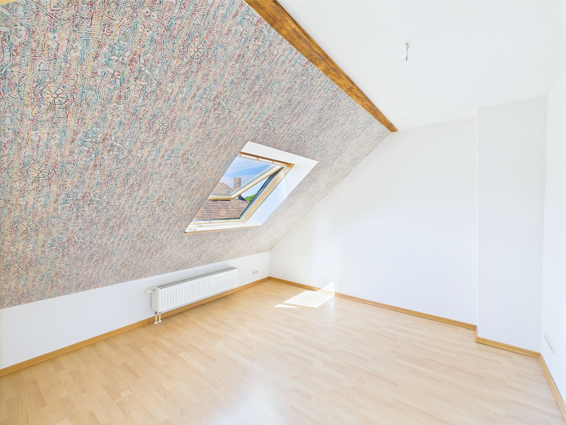 Helles Dachzimmer mit schräger Decke, Dachfenster und hellem Laminatboden.