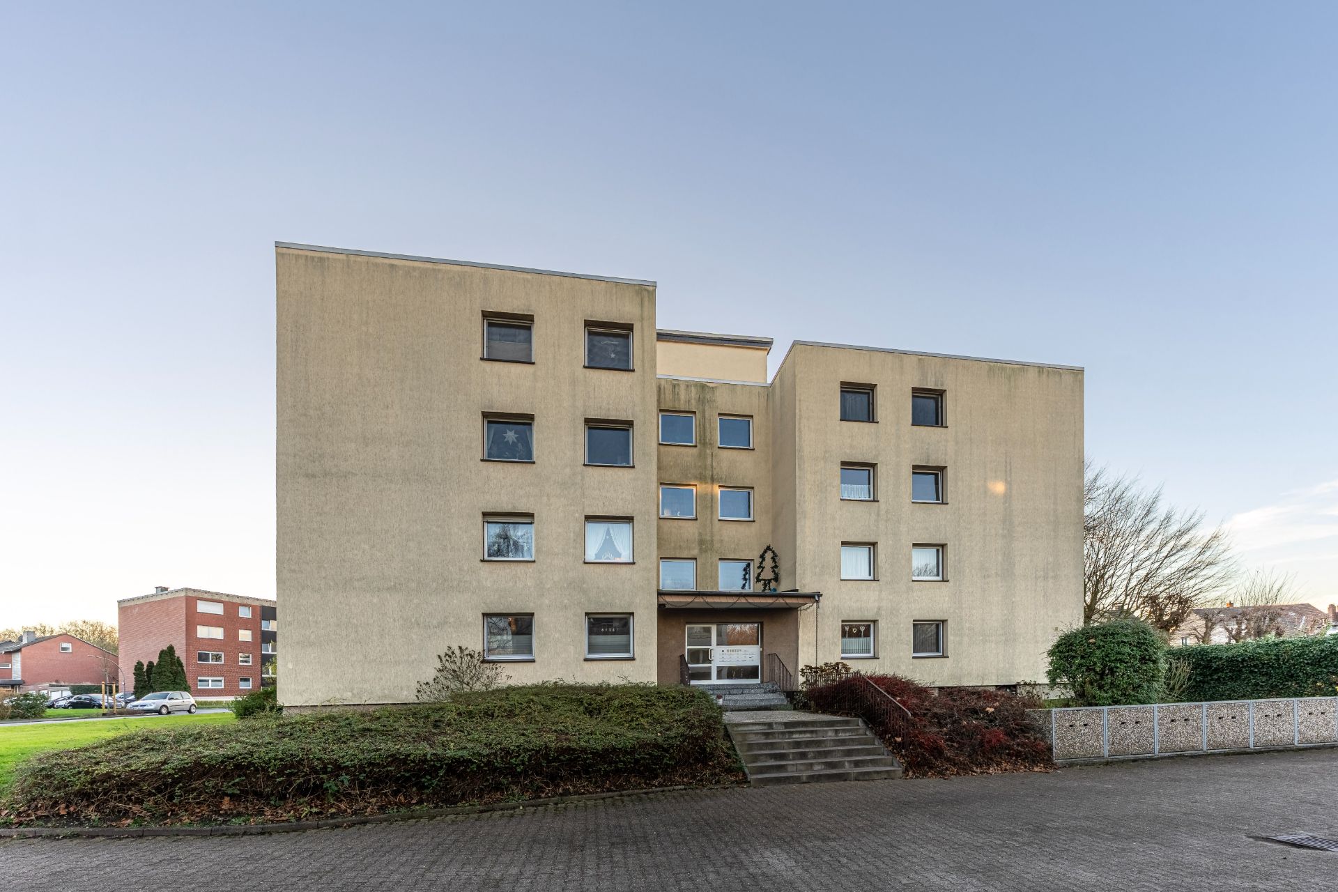 Mehrfamilienhaus mit drei Etagen, zentralem Eingang und umliegenden Grünflächen.