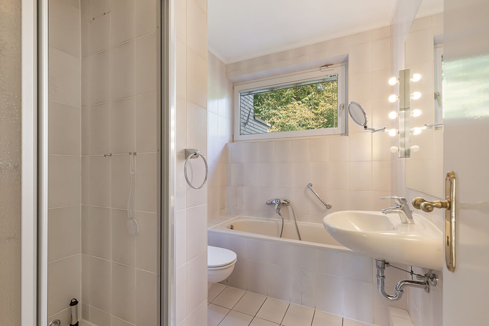 Helles Badezimmer mit Dusche, Badewanne, Waschbecken und Fenster.