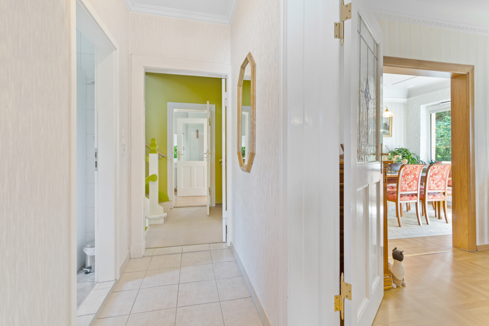 Heller Flur mit Fliesenboden, offenem Esszimmer und grüner Wand im Hintergrund.